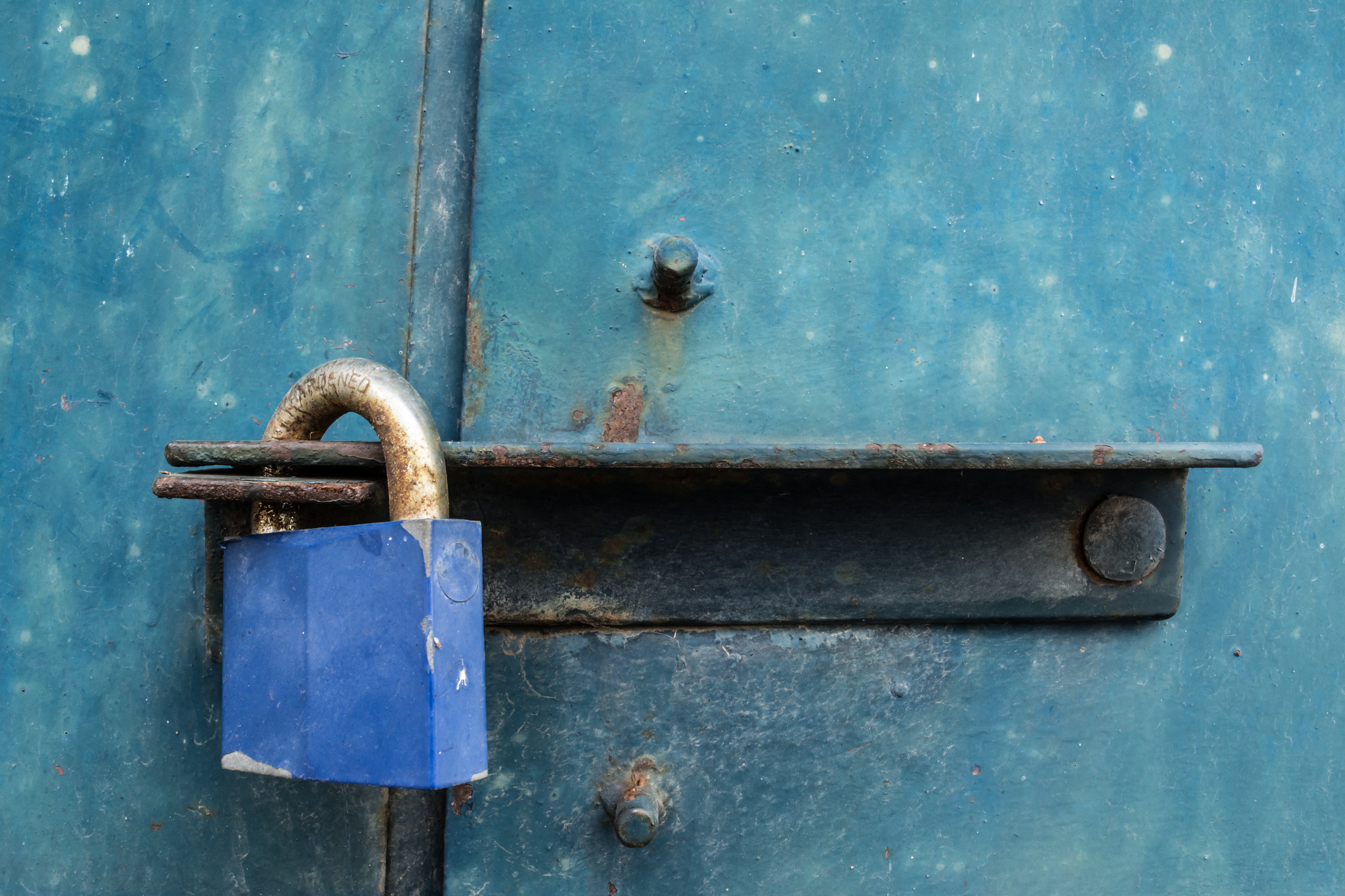 Blue padlock on rough, dirty iron door.
